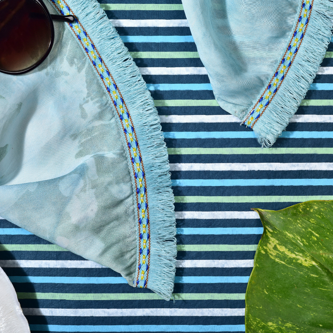 Cyan Swash scarf on striped blue background with decorative fringe and leaf accent, evoking a serene aesthetic