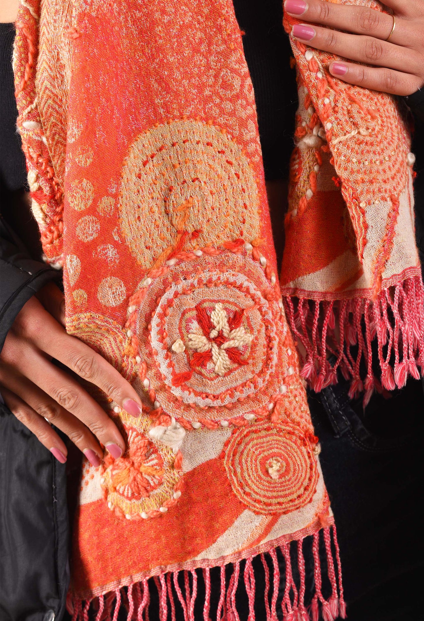 Close-up of detailed embroidery and fringe finish on an orange camel wool stole.
